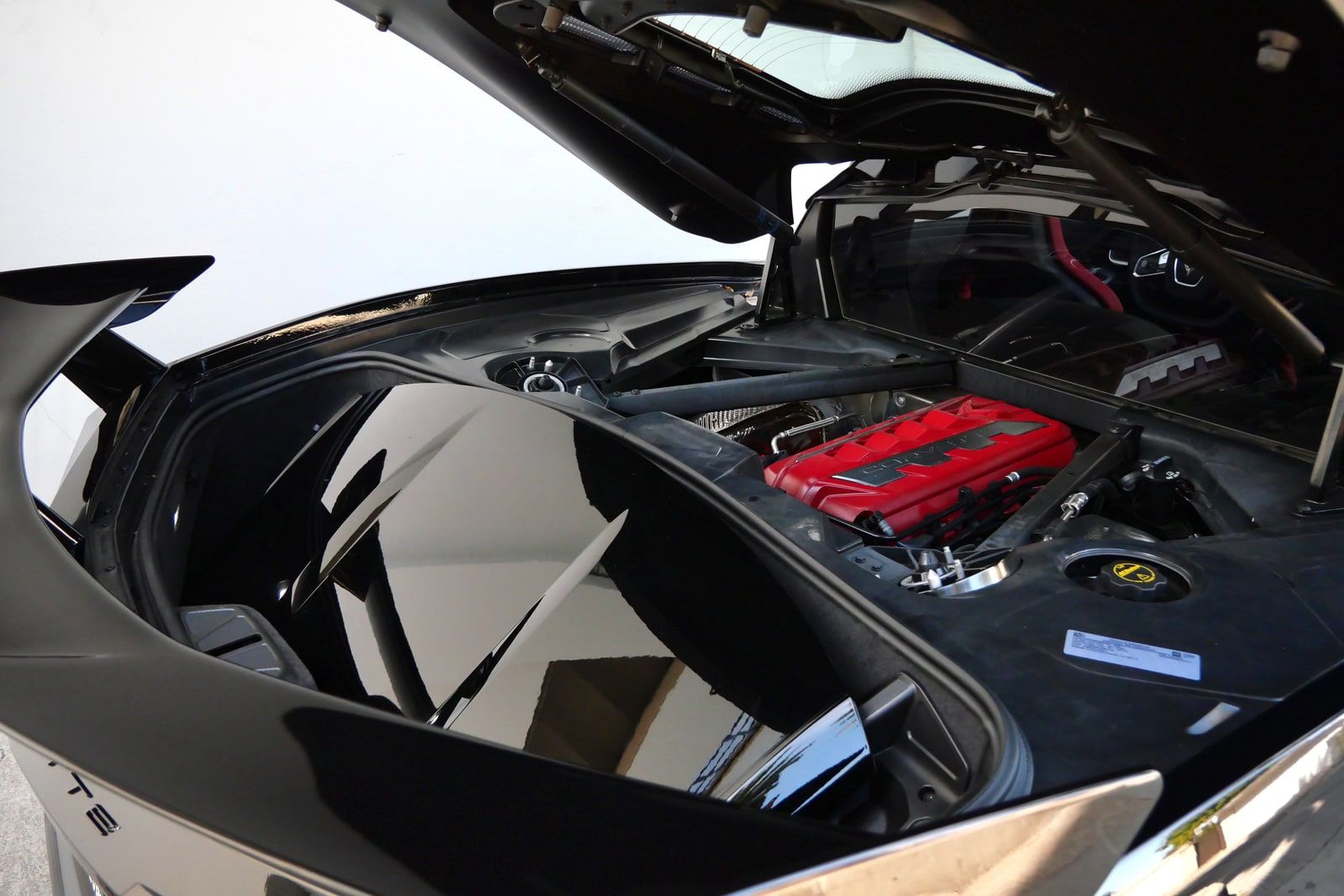 Rear glass hatch of a black Chevrolet Corvette C8 coupe raised to show the 6.2-litre V8 with its red engine cover