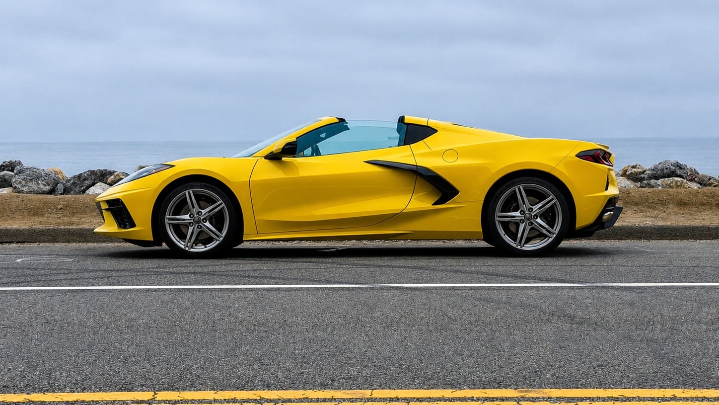 Yellow Chevrolet Corvette C8 in profile with the roof panel removed, ocean behind