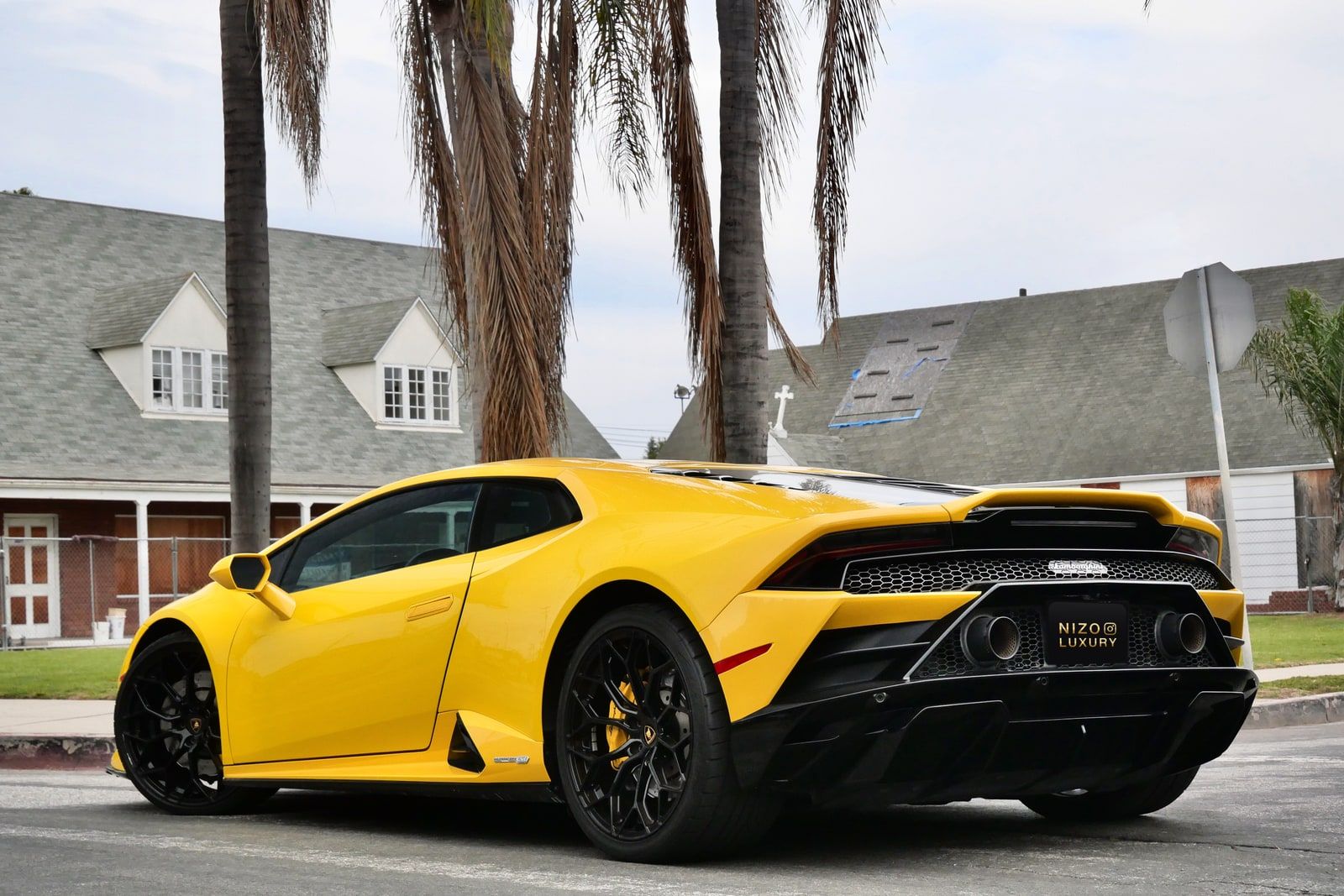 Yellow Lamborghini Huracán Evo seen from the rear three-quarter beneath palm trees