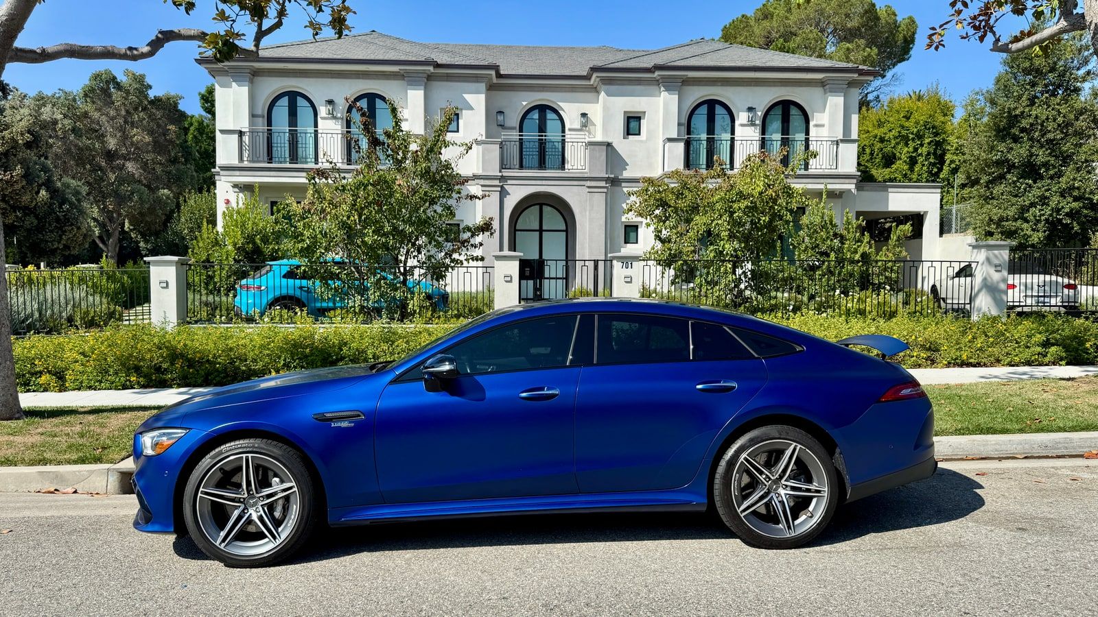 Satin blue Mercedes-AMG GT 43 four-door fastback in profile on a Beverly Hills residential street, showing how low the car sits and the rear door handles