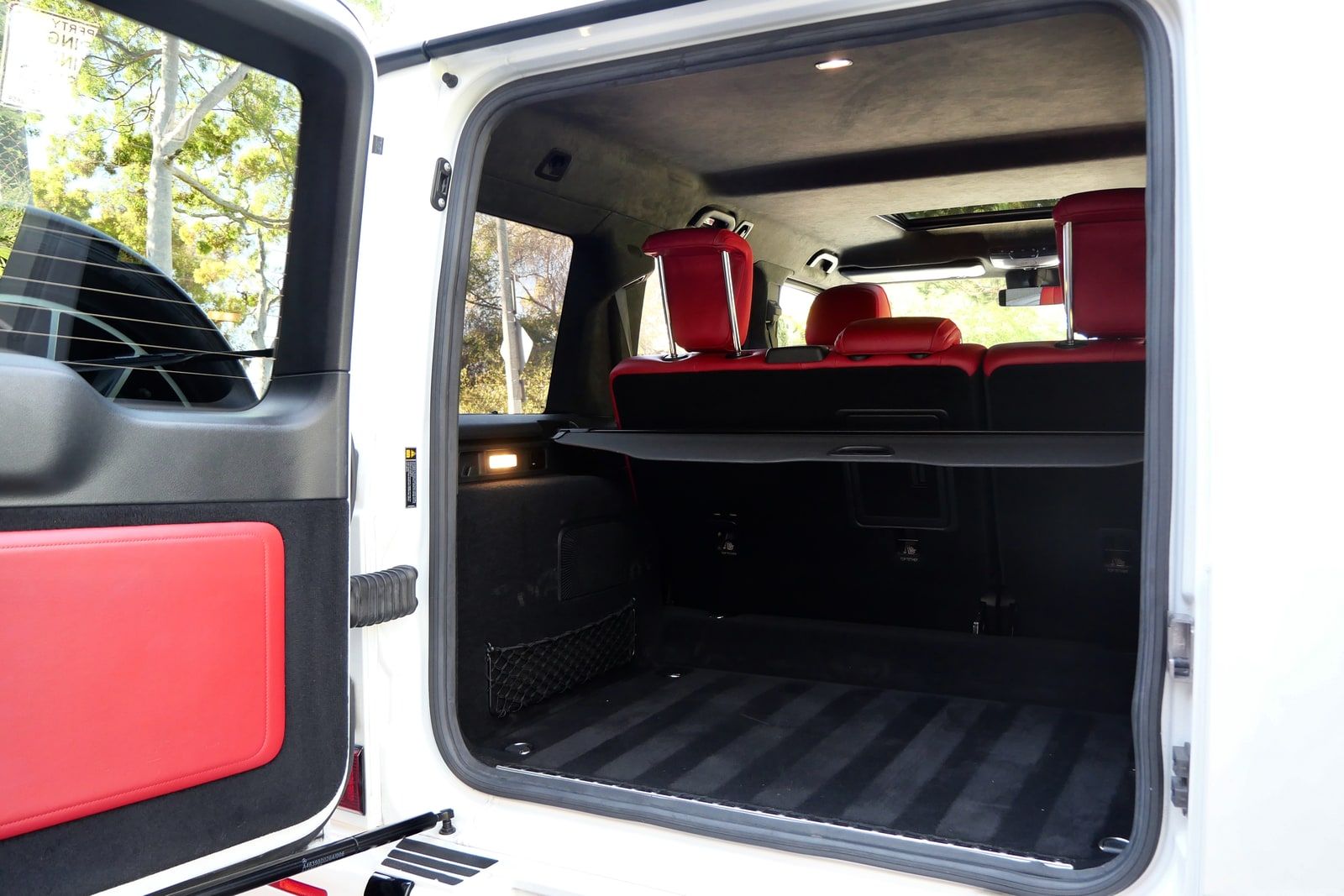 Rear cargo area of a white Mercedes G 550 through the open side-hinged rear door, with the red rear seats visible