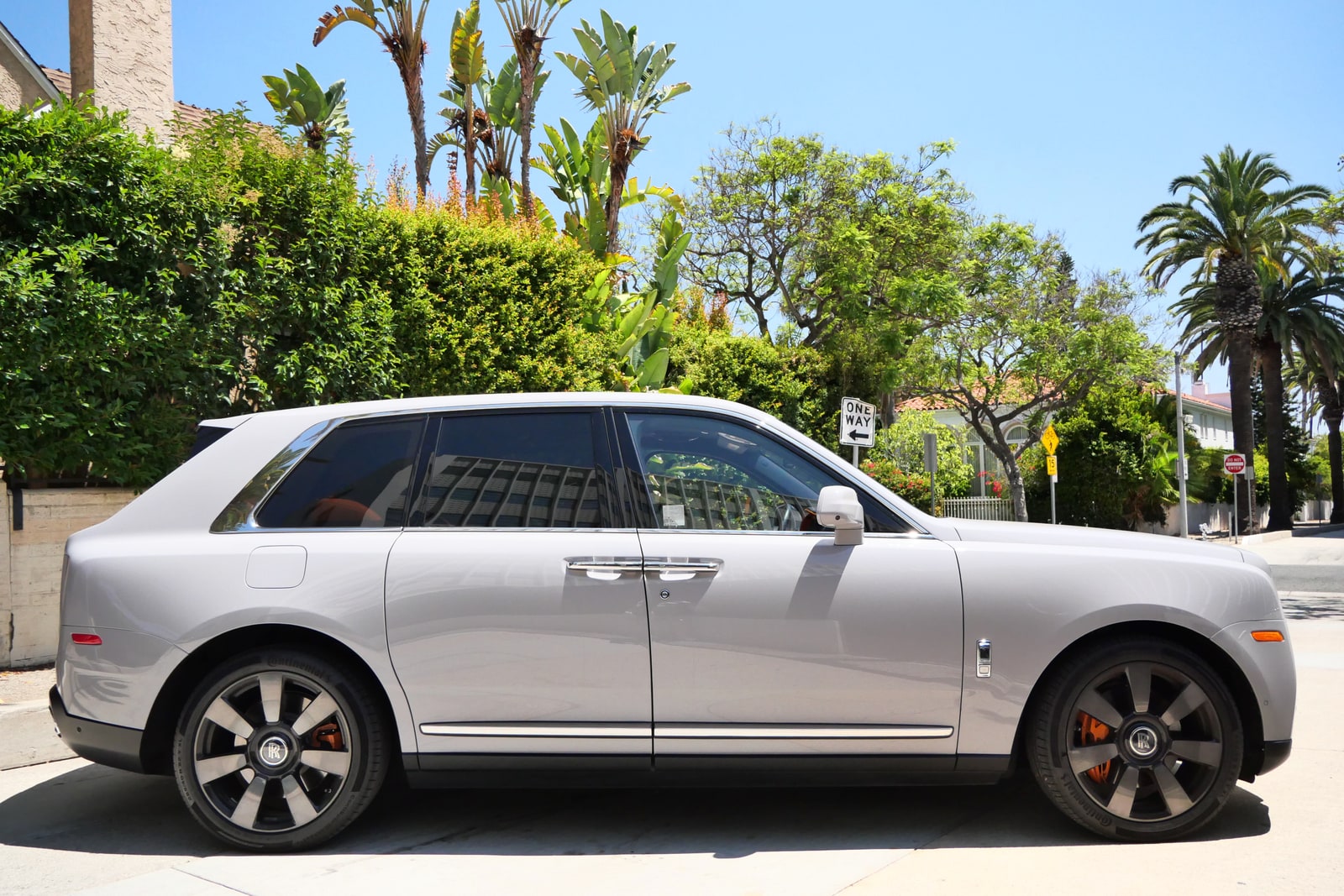 White Rolls-Royce Cullinan on a tree-lined Beverly Hills street, rear three-quarter view