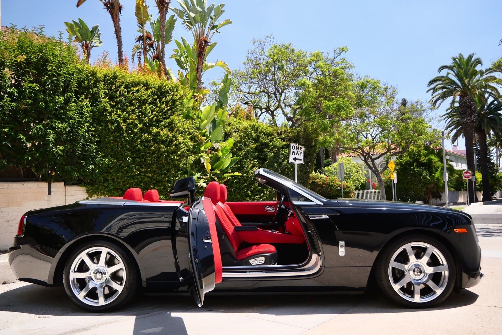Black Rolls-Royce Dawn convertible in profile with its roof down and both coach doors open, showing the red leather seats