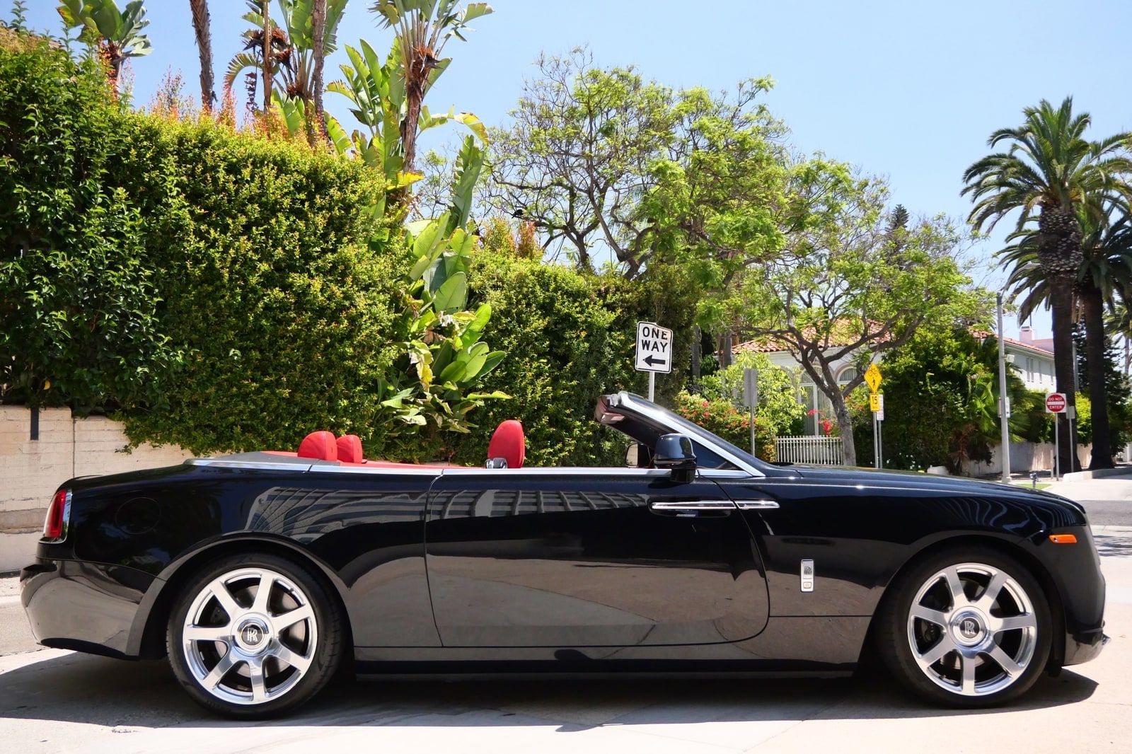 Black Rolls-Royce Dawn convertible with its roof down in profile on a palm-lined Los Angeles street