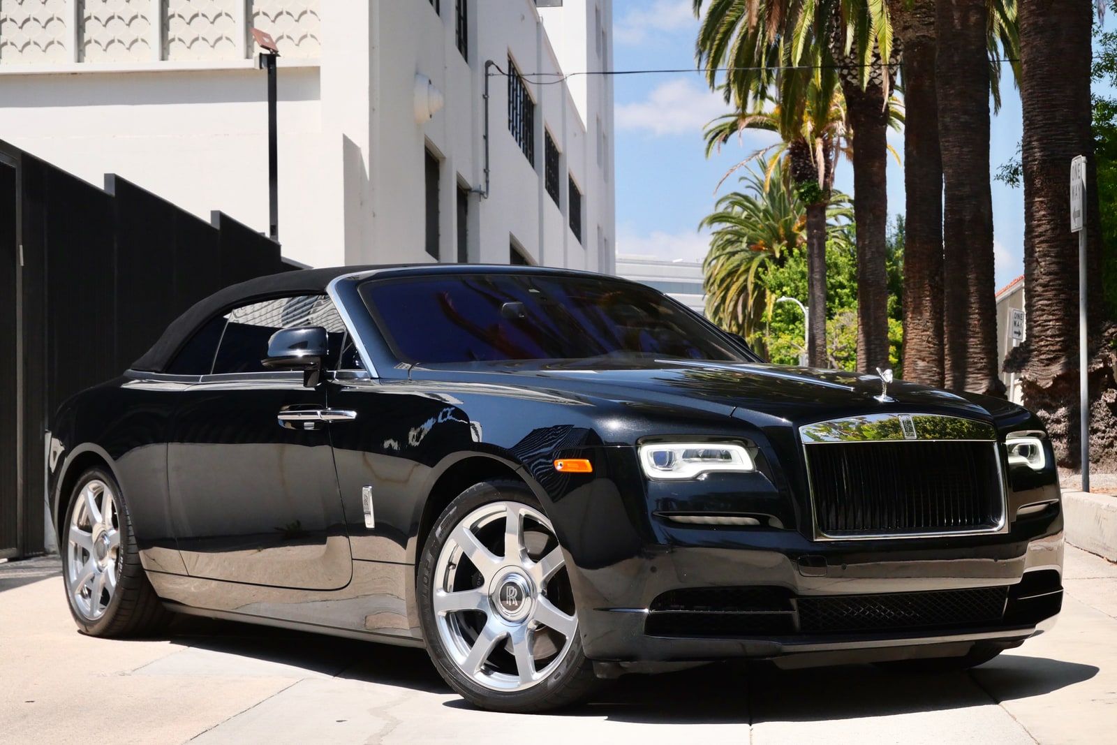 Black Rolls-Royce Dawn parked at a kerb with its roof down, rear three-quarter view