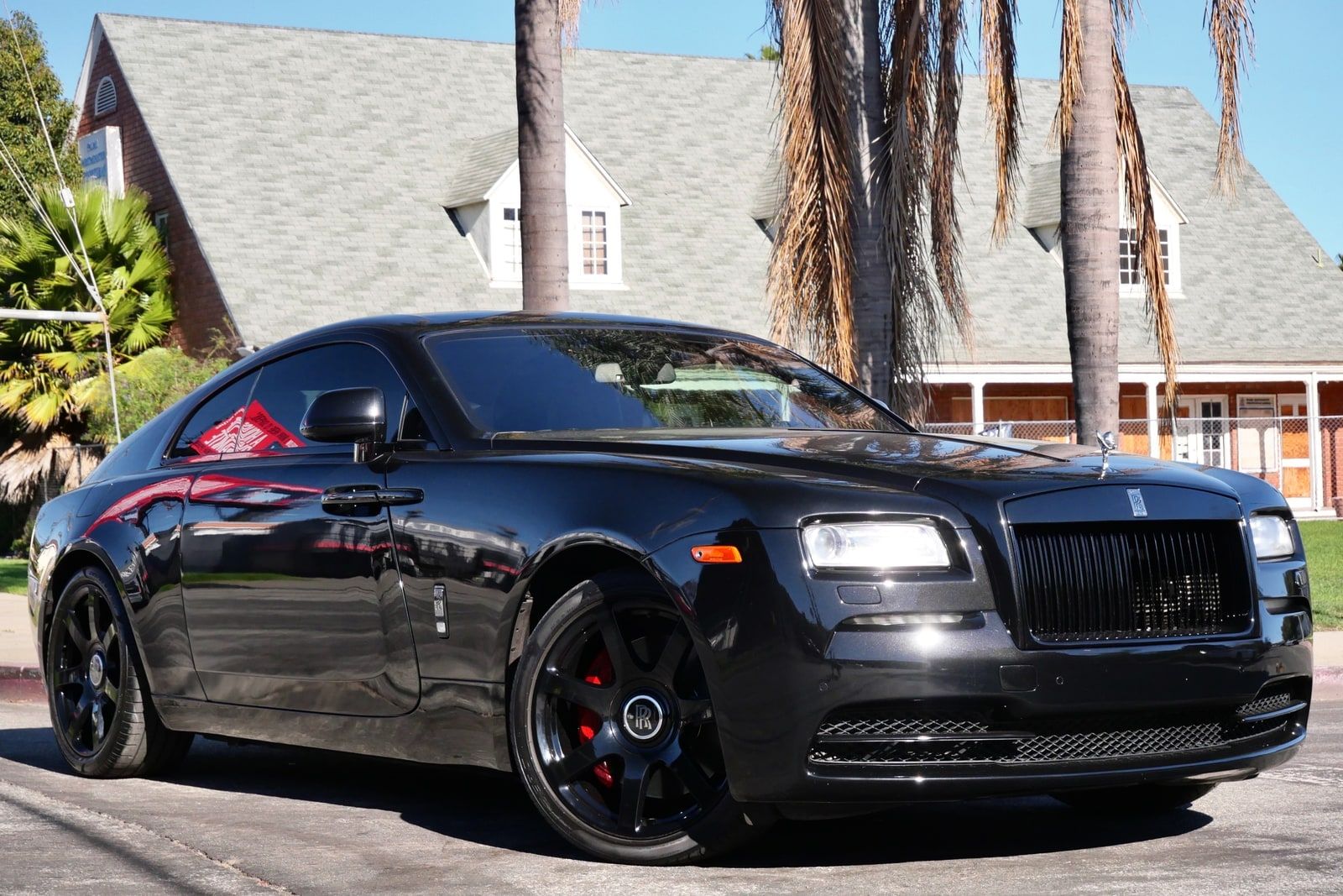 Black Rolls-Royce Wraith seen from the front three-quarter beneath palm trees